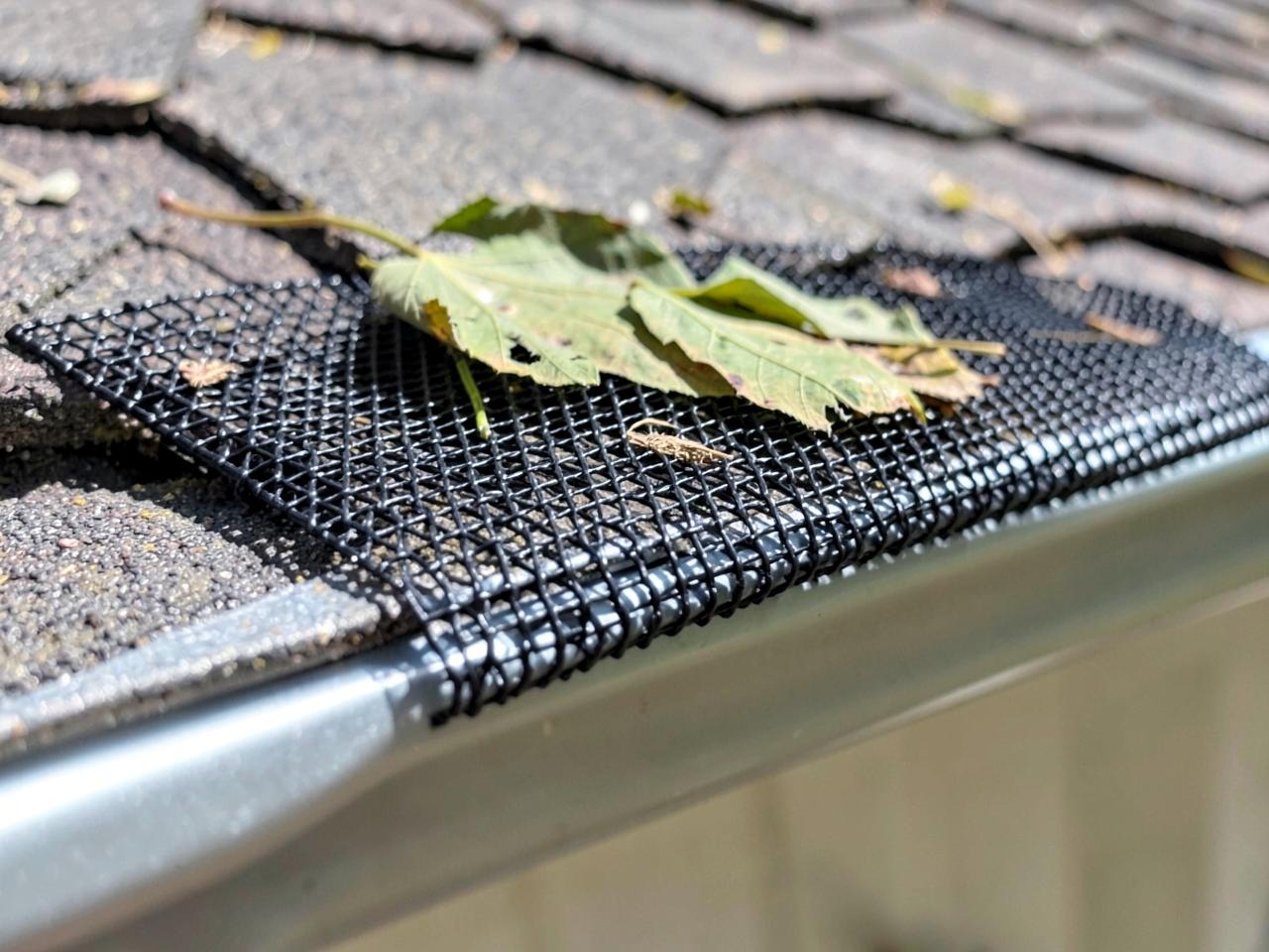 Black micro-mesh gutter guard fitted over an aluminum gutter with leaves resting on top