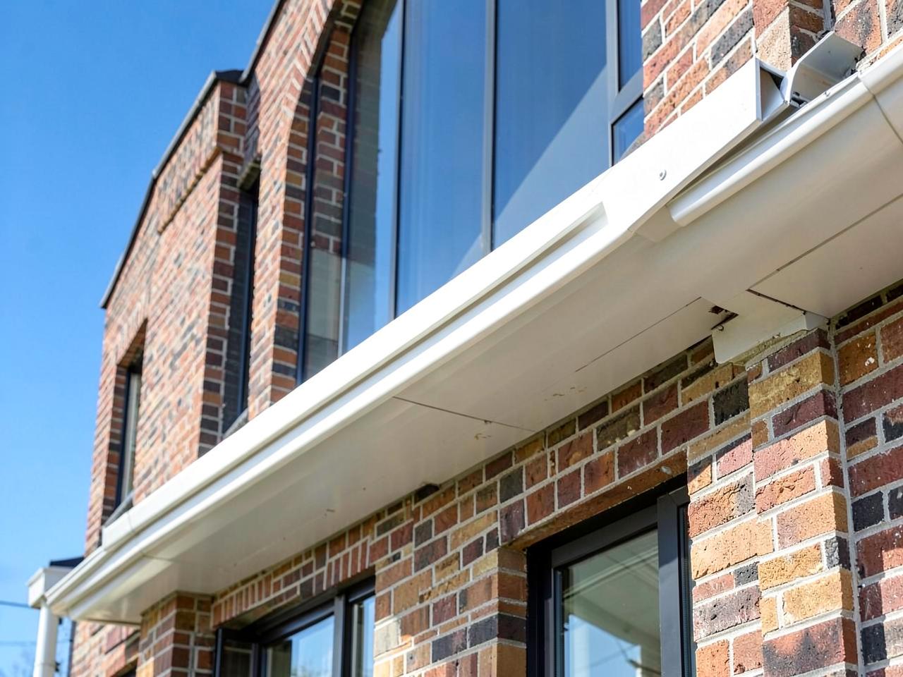 Newly installed seamless white aluminum eavestrough along the fascia of a brick home